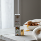 Lip balm packaging on a wooden surface with a bowl of honey and almonds in the background.