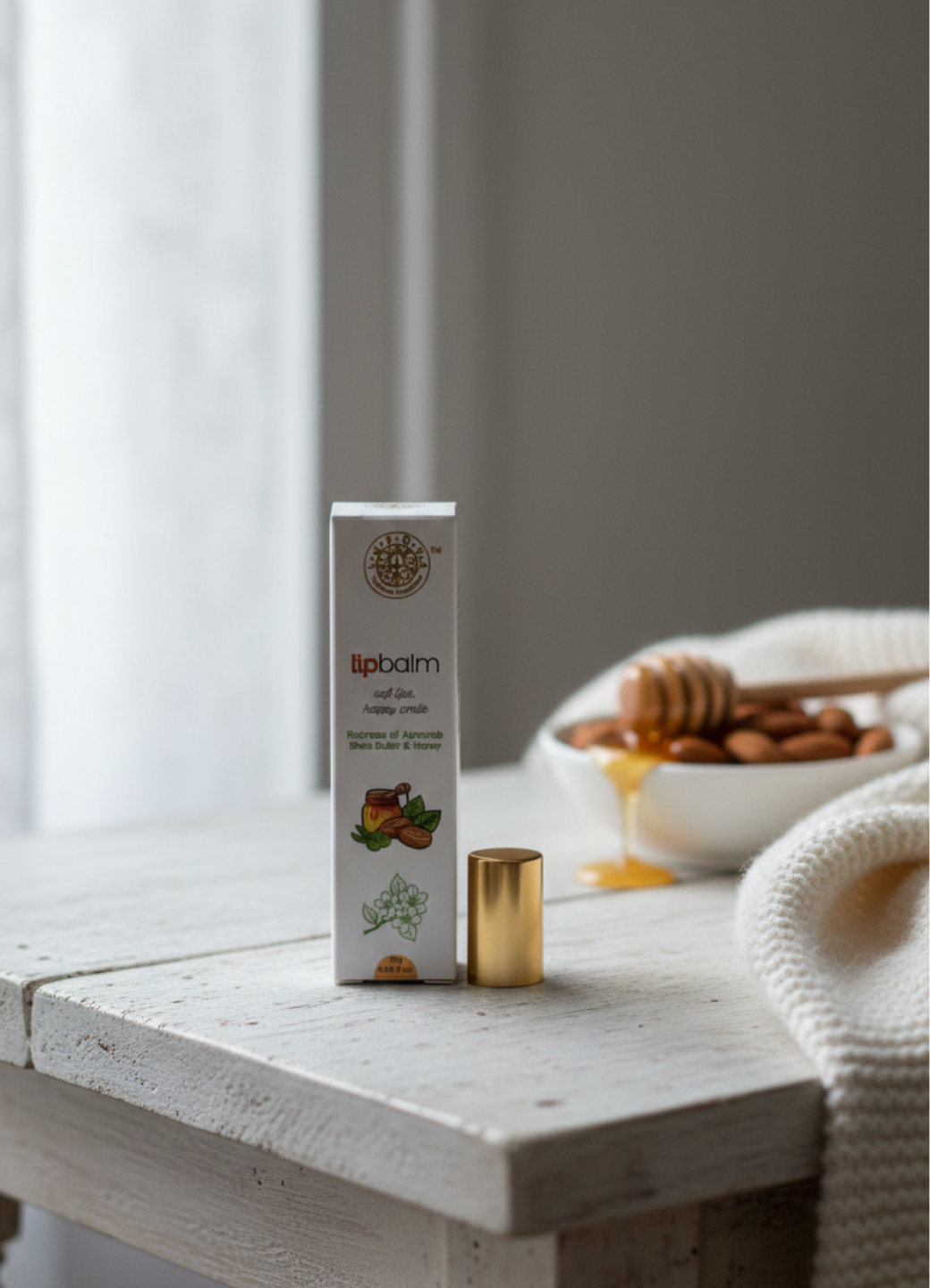 Lip balm packaging on a wooden surface with a bowl of honey and almonds in the background.