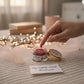 Hand applying a product from a jar labeled 'My nightly ritual' on a textured surface with blurred lights in the background.