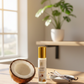 Coconut oil bottle, half-coconut, and vanilla beans on a wooden surface with a plant in the background.